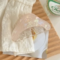 Détail d'une grande pince à cheveux rose nacré aux courbes douces sur tissu blanc - Jaune