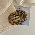 Detail of tortoiseshell acetate hair claw clip with golden logo on soft knit fabric - Dark Leopard Print