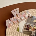 Detail showing wavy acetate hair claw clip with pink marble texture and gold logo stud - Light Pink