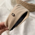 Dettaglio del cerchietto imbottito beige con emblema dorato e morbida trama in velluto - Cachi