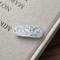 Macro detail of oval acetate hair clip with grey marble texture and gold handmade logo - Textured White