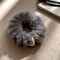 Macro shot of fluffy grey faux fur scrunchie featuring a reindeer label on soft felt surface - Gray