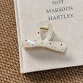Close-up of a cream bow hair claw clip with colorful rhinestones on a textured book - Bow Claw Clip