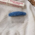 Close-up of a blue plush oval hair comb accessory with silver metal teeth on white fabric - Blue