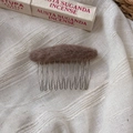 Detail of a brown plush oval hair comb with 10 metal teeth on a white textured fabric - Pink