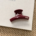 Detail of burgundy hair claw clip with golden logo on beige canvas background - Short Curved Style