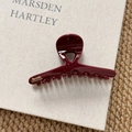 Dettaglio della molletta per capelli rosso scuro con logo dorato su un libro chiaro - Stile Incrociato