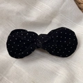 Detailed view of black velvet bow hair clip with white polka dots on beige fabric - Black