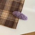 Detailed close-up of a soft purple plush hair clip on a vintage brown plaid fabric - Oval / Purple