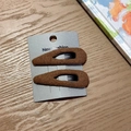 Close-up of a pair of brown fabric-wrapped drop hair clips on a warm wooden surface - Brown