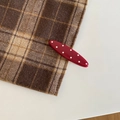 Close-up of a retro red oval hair clip with white polka dots on a checkered fabric background - Oval