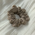 Dettaglio scrunchie marrone a righe con trama in lino su sfondo di stoffa bianca - Cachi