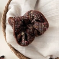 Détail d'un chouchou en tweed avec tissage à carreaux vintage et pendentif logo doré - Chouchou