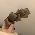 Dettaglio di un fermaglio per capelli con fiocco in raso marrone tenuto con eleganza - Caffè Chiaro
