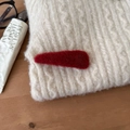 Close-up of a red plush hair clip texture pinned on a white knitted winter sweater - Triangle Style