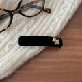 Detail van een fluwelen BB-haarclip met gouden hondenembleem op een witte gebreide trui - Zwart