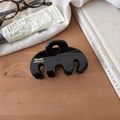 Detail view of a large black glossy hair claw clip on a rustic wooden table setup - Black Curved
