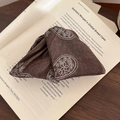 Close-up of a dark coffee brown paisley fabric hair clip on a vintage open book - Brown