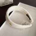 Detalle de diadema de vellón crema con emblema dorado y textura suave de felpa gruesa - Blanco Roto