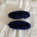 Detail showing a pair of navy blue plush fleece hair clips on a white fabric background - Dark Blue