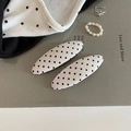 Dettaglio di due fermagli per capelli beige a pois su un vassoio espositivo strutturato - Bianco Ovale
