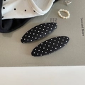 Close-up of a pair of black fabric hair clips with white polka dots on textured background - Black Oval