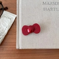 Gros plan d'une pince à cheveux nœud rouge brillant posée sur un livre de décoration - Style Nœud Arrondi