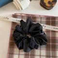 Detailed close-up of a large black matte satin scrunchie with ruffled edges on a fabric mat - Black