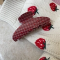 Detail der rot-weiß karierten Erdbeer-Haarklammer auf weißem Strickhintergrund - Sichelstil / Rot Weiß Gingham Erdbeere