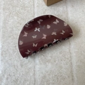 Close-up of deep red butterfly hair claw clip with silver spring on beige stone texture - Brown Semicircle