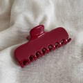 Macro shot of deep red acetate hair claw clip showing glossy finish on beige linen - Red