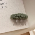 Macro shot of green faux lamb wool hair comb detail with metallic teeth on book surface - Green