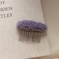 Close-up of lavender faux fur hair comb on a book showing soft texture and metal teeth - Purple