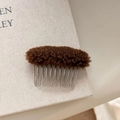 Detail of a brown fuzzy plush hair comb with ten silver metal teeth on a book background - Brown
