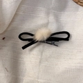 Detail of a black velvet bow hair clip with a soft beige plush ball on fabric - Black Bow Hair Clip