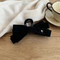 Detail of a black velvet bow hair claw with a small silver heart charm on a wooden table - Black