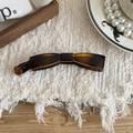 Detail view of a vintage amber resin banana hair clip on a decorative tray - Amber Rectangular Shape / Yellow Tortoiseshell
