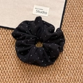 Dettaglio di un elastico in maglia nera a pois bianchi su un tappetino intrecciato - Nero