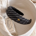 Gros plan détaillé d'un serre-tête en tricot rayé avec étiquette en métal doré fait main - Noir