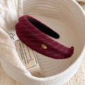 Détail d'un serre-tête rayé bordeaux avec une étiquette métallique dorée Hand Made - Rouge