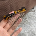 Macro view of 10-tooth metal hair comb with amber acetate bow in hand against fabric - Dark Tortoiseshell