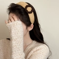Detail view of knitted velvet headband with round floral ornament on a model's hair - Turmeric