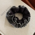 Detail shot of black knit scrunchie with striped silk-textured ruffled edges on a table - Black