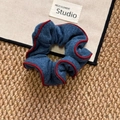 Blue denim fabric scrunchie with red piping edges on a neutral textured background - Blue Scrunchie