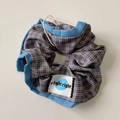 Vista dettagliata del grande elastico per capelli a quadretti blu e marroni con logo - Scrunchie Plaid Bordo Blu