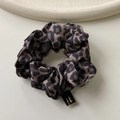 Détail d'un chouchou léopard en soie avec texture satinée lisse et étiquette noire fine - Imprimé léopard