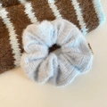 Macro view of light blue knitted scrunchie showing soft texture and brand label - Blue