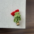 Detail of a handmade knitted Christmas hair clip with a red bow on a textured background - Christmas Curly Tree