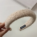 Detalle de la diadema beige de lana de cordero con etiqueta artesanal y textura suave - Caqui