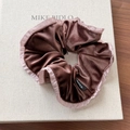 Detailansicht Samt-Haargummi in Braun mit rosa Plissee-Rand auf Buch-Hintergrund - Rosa Scrunchie